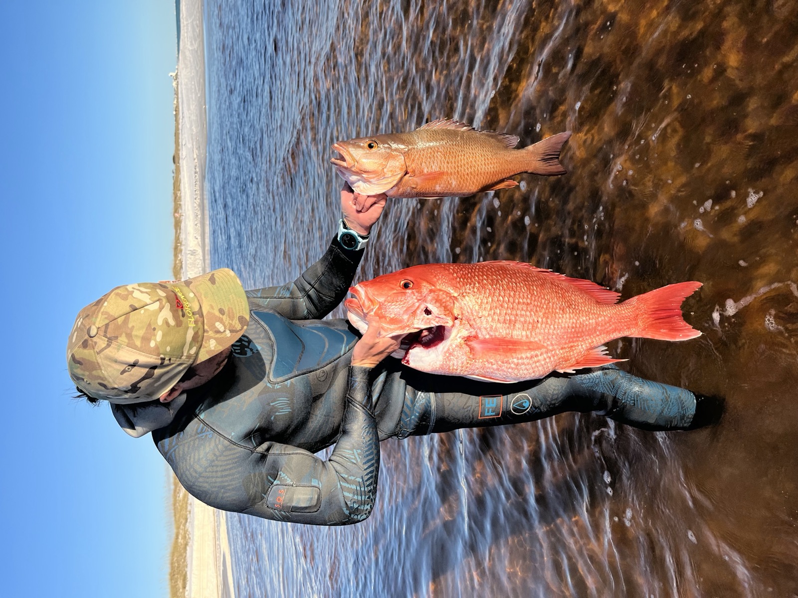 Kyle holding two fish in the shallow water by the beach